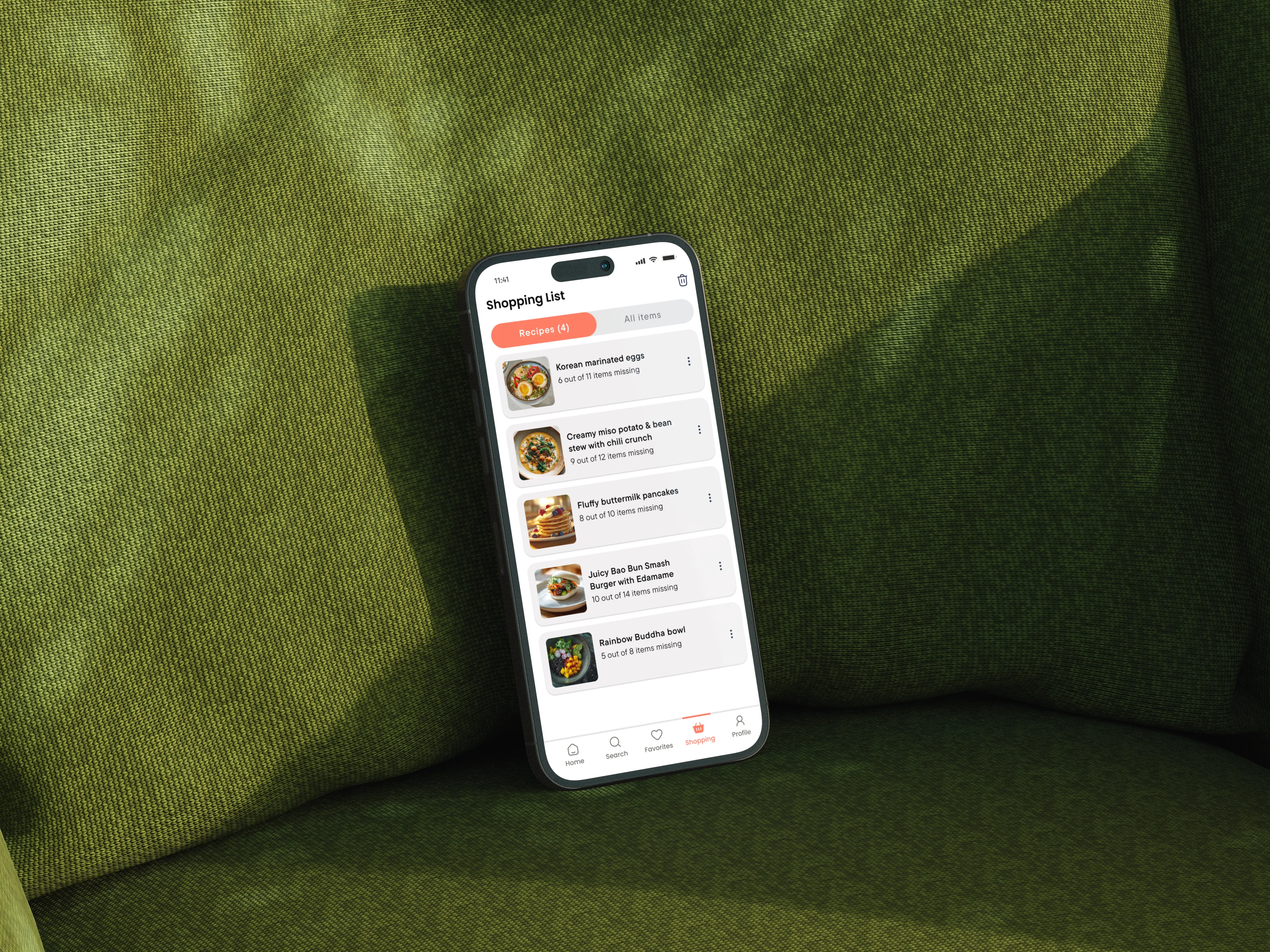 Dishcovery Shopping List screen on a phone leaning against a green textured couch